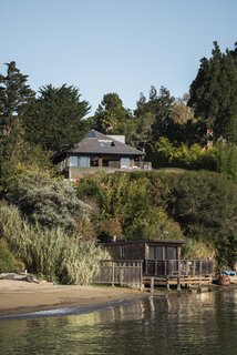 The property, situated on a steep bluff overlooking the San Francisco Bay, includes a main house with a deck, a pool, an outdoor kitchen, and a boathouse. 