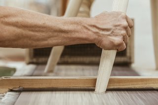 Watch: It Takes 9 Hours For Woodworkers to Make This Shaker-Inspired Chair - Photo 19 of 19 - Level the Legs: A 24-inch belt sander levels the legs—the last step before the chair is taken to the finishing department. There, warm oil is sprayed on to protect the wood. Finally, wax is hand-applied and then buffed to create the finish.