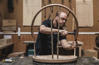Watch: It Takes 9 Hours For Woodworkers to Make This Shaker-Inspired Chair - Photo 16 of 19 - Build: Starting with the longest and shortest lengths, artisan Warren Shaw taps the ash spindles into the top of the seat and the continuous arm with a mallet. The legs will follow. 