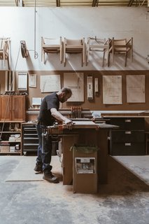 Watch: It Takes 9 Hours For Woodworkers to Make This Shaker-Inspired Chair - Photo 1 of 19 - At the workshop in Auburn, Maine, master craftsman Warren Shaw glues and clamps together three pieces of cherry to make a panel that will form the seat of a Continuous Arm Chair. The artisans sometimes call the piece "TMC"—Thos. Moser Continuous—for short.