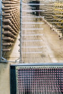 <b>3 Wind The Warp </b> Before weaving the pattern, weavers at the mill must prepare the warp, which creates the vertical structure of the fabric. Here, a "creel" holds hundreds of cones of yarn that will be used to start building the warp. 