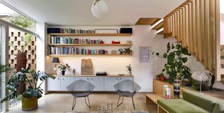 Open shelves and sleek cupboards line one wall of the living room. The floor-to-ceiling glass door leads to the exterior courtyard, which is bounded by the perforated brick wall.