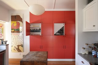 Architect Eric Schiller built storage units underneath the stairs in the kitchen and had them painted Geranium by Benjamin Moore. Old Herman Miller posters hang on a nearby wall.