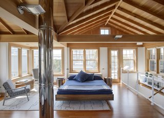 The sun-filled second story, which serves as the master bedroom and lounge, is pierced by a metal chimney. The Fusion bed by Zeitraum is flanked by nightstands by Robert Kuo and lamps by Cedric Hartman from the 1960s. A custom Moroccan rug covers the floor. A pair of refinished midcentury Danish chairs sit beside a Hans Wegner chest.