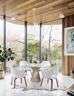 Cover Story: This House in Austin Has a Tree Growing Right Through It - Photo 5 of 10 - Because the property slopes to the rear, the home’s eastern view is of treetops right outside. In the dining nook, Executive Armchairs by Eero Saarinen join a Warren Platner table beneath a Serge Mouille ceiling light. A patterned rug by AVO rests on the terrazzo tile floor. 