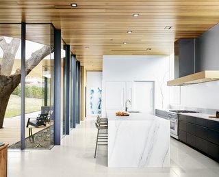 Cover Story: This House in Austin Has a Tree Growing Right Through It - Photo 6 of 10 - Chris, a retired commodities derivatives trader, served as the general contractor, with guidance from builder Mike Paulsen. Decorum Arch Stone fabricated the waterfall countertop made of Colorado Gold marble; Scott Cabinets did the millwork. The cooking range is by Wolf. Trove wallpaper accents the far wall of the powder room at the end of the corridor. 