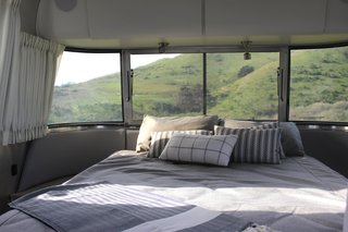 Panoramic windows allow the lush hills to act as our headboard, while blackout curtains ensure a good night's sleep. Low-profile nightstands and overhead cabinets offer additional storage.