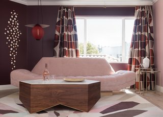 Designer Melanie Coddington of Coddington Design tranformed the family room into her "Unapologetically Pink Rosé Lounge." Inspired by edginess and fueled by French rosé wine, the lounge is modern, opulent, and without a doubt, unapologetically pink. The lounge revolves around a geometric marble and walnut cocktail table with brass inlaid rings to mimic wine stains. Nearby sits a midcentury-style gondola sofa with custom fabric and a classic American 1950s swivel chair.