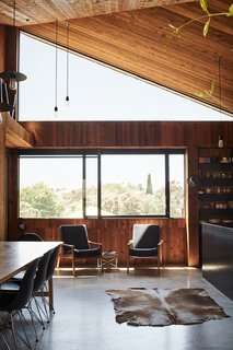 The kitchen/dining room is lined in knotty cedar planks. A pair of Danish modern chairs face <br>a cowhide rug—a family heirloom.