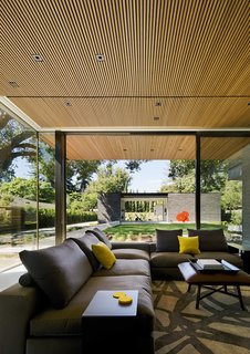 Bracketed on one end by glass, the living room captures a view through the guesthouse breezeway to the cypress trees beyond. The sculpture "Big Red Poppies" by Donald Sultan provides a pop of color on the lawn.