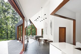 The communal area enjoys a close connection to the outdoors through a Duratherm lift-roll door. Beneath artworks by Christopher Flach, Cherner armchairs are paired with a Tulip table from Knoll. 