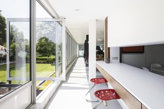 A pivoting glass door leads from the second-story kitchen to an elevated terrace and onto the lawn. The Mezzadro stools are by Achille and Pier Giacomo Castiglioni.