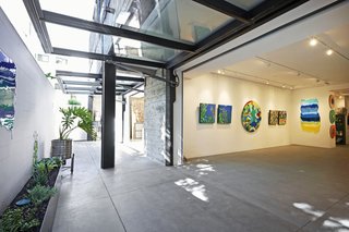 Recalling the drive-in openings of the former auto shop, hydraulic glass garage doors hang from both Klari’s studio and the exhibition space, where a selection of her paintings is on view.