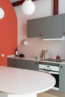 The kitchen cabinets are finished in a warm gray, and are fitted with vintage, brass concave handles.