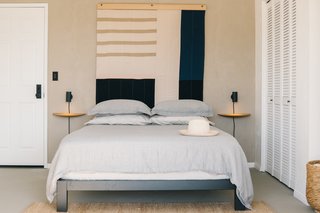 The master bedroom is a peaceful retreat against a backdrop of a Louise Gray wall tapestry, wall sconces from Rich Brilliant Willing, and Menu Fungi Shelves. Snowe linens outfit the bed, which boasts an Avocado mattress, and the Nest Rug is from Armadillo & Co.