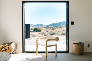 The living room frames the desert landscape through LaCantina doors. A WAKA WAKA Cylinder Back Arm Chair made from birch plywood adds warmth and character to the space. 