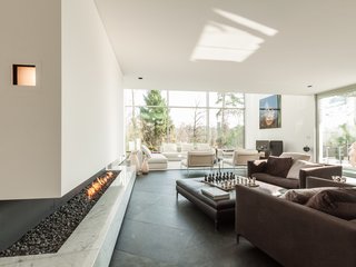 Built in 2011, this six-bedroom, five-bath villa in Brussels offers an array of spaces complete with high ceilings, expansive terraces, and a meticulously landscaped garden. Running adjacent to a wall of floor-to-ceiling windows is a cut-in stone fireplace that lies beneath a glass-enclosed walkway. 