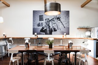 The base of the communal table is from Restoration Hardware while the custom copper table top is by Chris Mast. The restaurant is centered underneath a metal drum pendant light from Restoration Hardware and is finished with an authentic Greek photo-mural titled, The Guy in the Room by Nikos Economopoulos. 