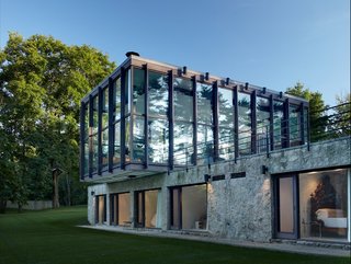 Shown here is a view of the stone and concrete structure that supports the cantilevered glass pavilion. The bottom section holds four bedrooms, bathrooms, and a sitting room. The glass and wood pavilion on top houses a combined living, dining, and kitchen space—all which is surrounded by 15-foot-tall windows. 