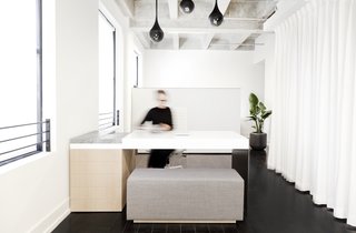 The custom appointment desk was designed and built with a single bent sheet of aluminum, lacquered MDF, marble, and white oak. The floor-to-ceiling white curtain hides the built-in kitchen that was part of Lee's loft from the beginning.