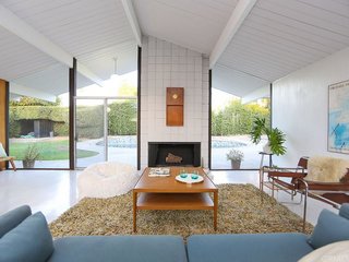 The living space—which looks past a fireplace and out to the pool—sits under original beamed ceilings with a characteristic A-frame shape.