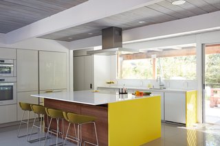 Same Bones, New Materials—A Double Gable Eichler Gets a Dashing Update - Photo 5 of 9 - The new gray porcelain tiles are fit together seamlessly throughout the space and into the courtyard. The more open kitchen now has a wall of built-in storage and an oversized island with walnut and a brightly-colored siding. 