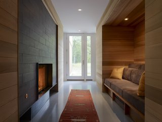 Red Cedar Is the Key Ingredient of This Wooded Cottage For Sale - Photo 7 of 8 - Entering through the front door leads you to an inglenook, where Lynch installed a fireplace and a custom built-in seating area that’s surrounded by red cedar. 