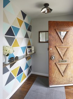 Carly and Brad rearranged the former entry closet area to create a small vestibule that would block the direct view to the kitchen upon arrival. Instead of covering it with wallpaper, they created a custom stencil and painted it themselves on Christmas Eve. They used the colors that can be found throughout the house, while the triangles take cues from the carvings on the original door. 