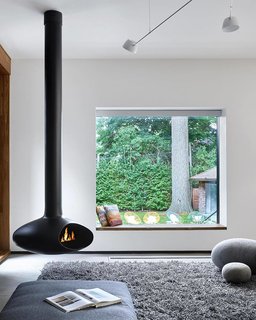 The living space that features a freestanding fireplace looks out through a seated window that perfectly frames the yard. 