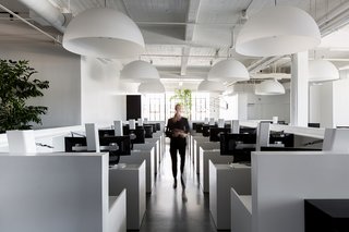 The central open work area is filled with white standing desks made by Muller Nichols, which sit under large dome pendants by FontanaArte.