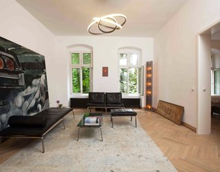 An antique floor lamp and signage pair with an oversize automotive painting and a rug by Rugstar in the main living space. The daybed and lounge chairs are from Norr11's Man seating collection; the pendant is from Cameron Design House.