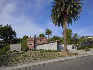A view of the completed renovation; from the street, the open amphitheater-style courtyard appears as a simple wooden addition, privately tucked away. Wood slats, exterior cladding, and the new trellis all combine to form a linear motif.