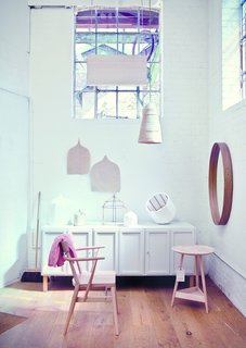 In the Pinch showroom, a Holland Park School armchair designed by Richard Pinch for Ercol sits beside a Clyde lamp table and Frey sideboard from the Pinch collection. The brand's Iona mirror hangs on the wall while their gauzy Beata pendant dangles from above. 