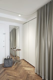 By the entrance, a silver curtains in KnollTextiles fabric hide a Poliform storage system and a Murphy bed. 