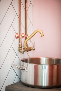 Rustic brass fixtures are attached to a wall of subway tile that has been arranged in a herringbone pattern.