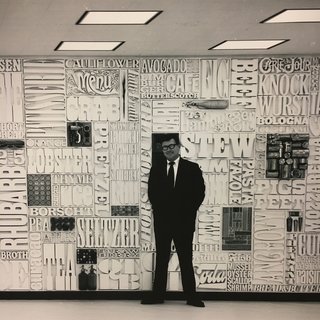 New York's Hidden
Graphic Design Gem - Photo 4 of 6 - Lou Dorfsman standing infront of "Gastrotypographical". With the help of Tom Carnase, Herb Lubalin worked extensively on this typographic "wall of words" that spanned 35 feet in width and 8 feet in height. It was situated in the cafeteria at the CBS headquarters in New York City. The concept was to treat the wall like a giant typesetter's case, with a lock-up of words and objects on the theme of food. 1966