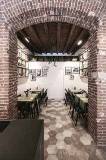 Bringing a Taste of
Sicily to Milan - Photo 3 of 5 - The dining space at the back of the restaurant showcases hexagonal tiles in varying shades of gray, as well as custom tables and black folding chairs designed by Studio DiDeA. The shelving units feature an assortment of Mediterranean products for sale. 