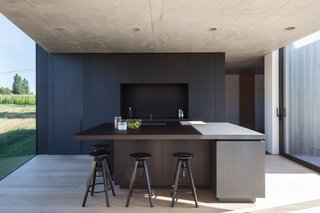 The building materials, have been guided by the vibrant colours of the rural landscape. Grey wood, patterned concrete and dark, anodised windows are the main components. The use of concrete is a wink to the historical nature of the surroundings and accentuates the massiveness of the building. Oak floors provide warmth to the interior and the kitchen area made of black-stained oak acts as a resting point. These basic colours make sure the focus is on what is happening outside, not inside.