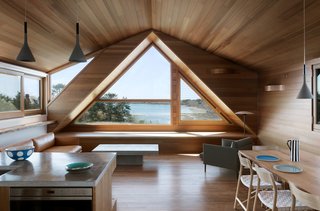 "Because the living room occupies the gable, the resultant space is triangular in feel," Thompson says. So she heightened that look with an oversized triangle window, which maximizes views of the cove. Western red cedar was chosen for the walls, and three-inch red oak was chosen for the interior floors. The windows are encased in Alaskan Yellow Cedar. 
