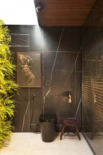 An Incredible Brazilian Home That Celebrates Art, Travel, and Nature - Photo 12 of 14 - The black toilet is nearly camouflaged against the marble-clad walls, while art and greenery stand out.