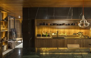 An Incredible Brazilian Home That Celebrates Art, Travel, and Nature - Photo 4 of 14 - The home’s kitchen marries a wood-slatted ceiling and wood cabinetry with marble counters.