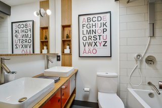 A remodeled bathroom favors white tile and finishes, with a quirky pop of color on the vanity.