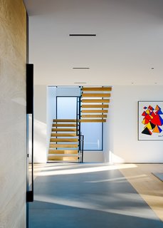 Intimately tied to the steep topography, views and experiences change as one travels through the home. Traveling up the steep entry to the living level on the second floor, the entry space offers access to both the living room to the north, and private dining and kitchen area to the south. Wide-plank European white oak flooring, and Pietra Serena limestone slab inlays bring an organic warmth to the space.