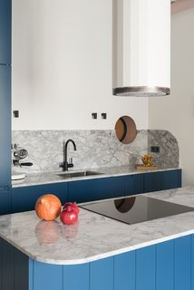 Soft curves and arches—a design move repeated throughout the apartment—are readily on display in the home's kitchen. A portal window to the bathroom, an arched marble island and backsplash, and a cylindrical Corinthia hood by Faber all add softly curved accents.