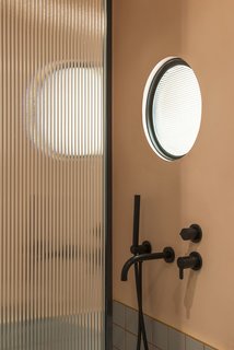 Optical glass, framed in matte black, features in both the shower screen and the circular portal window which adjoins the kitchen. It's a quirky touch that allows light to flow into the interior bathroom space.