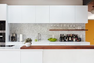A custom walnut slab bar counter and shelf, along with a hex tile backsplash, add pops of texture and depth to an otherwise clean and monochrome palette.