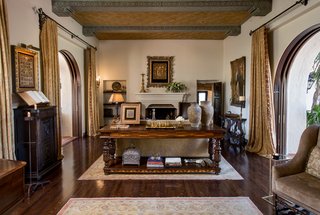 The main house showcases a great room with original gold-leaf ceiling panels and arched mahogany pocket doors, opening the entire home to the gardens and fountains.