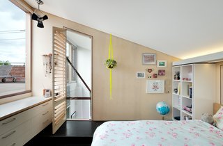 This little bedroom in a plywood pod looks out to the roof-deck and features angled ceilings and strategic lighting that's hidden above a shelving unit.