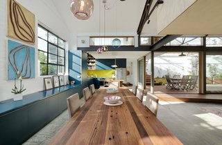 Custom cabinetry lines the dining area, which is defined by a large wood dining table and colorful glass pendant lights.