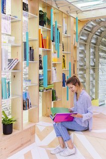 The "library" is designed with a shelving system that allows light to enter, opening up the narrow living space.